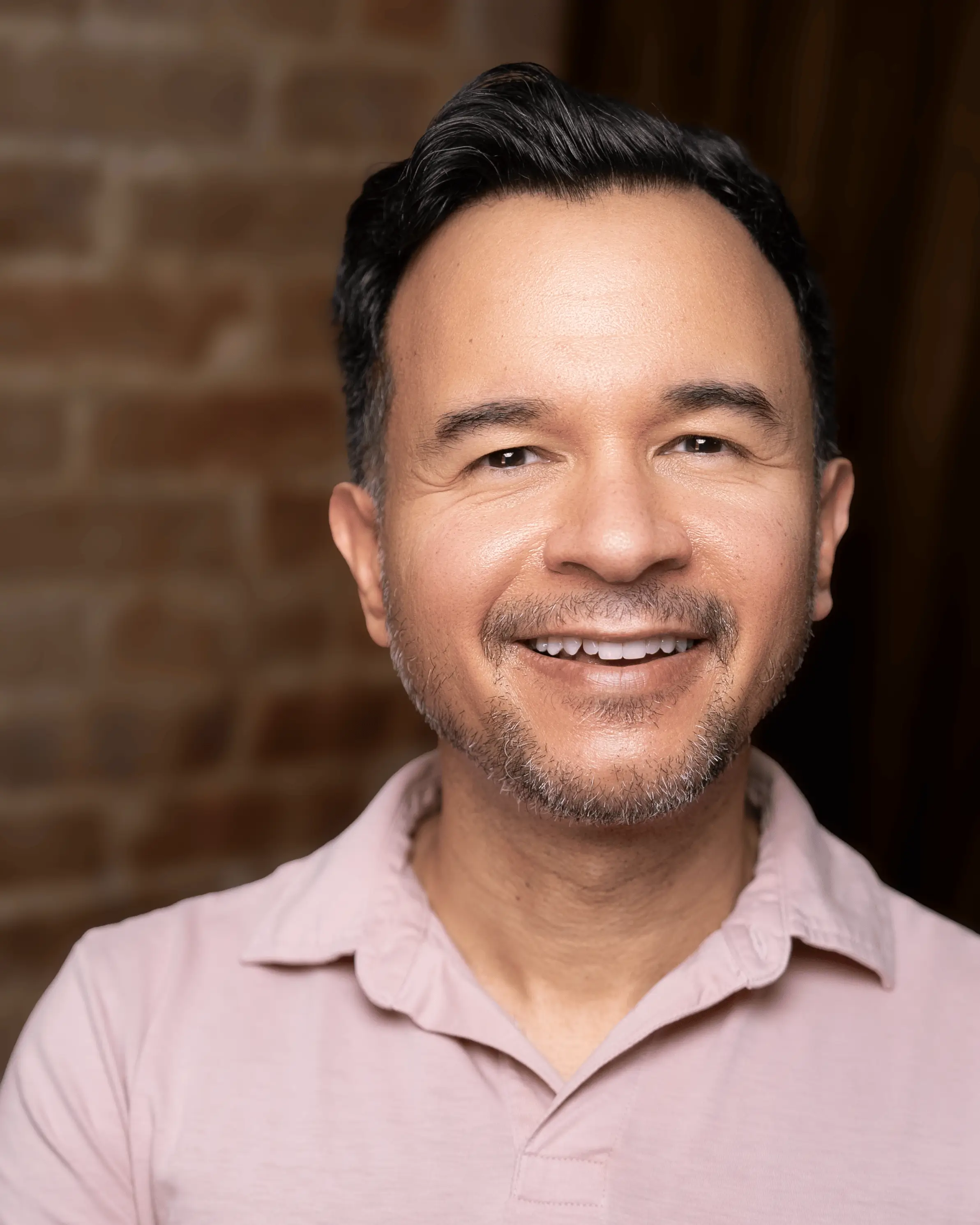 Portrait of Dr. Israel Martinez smiling in front of a brick wall