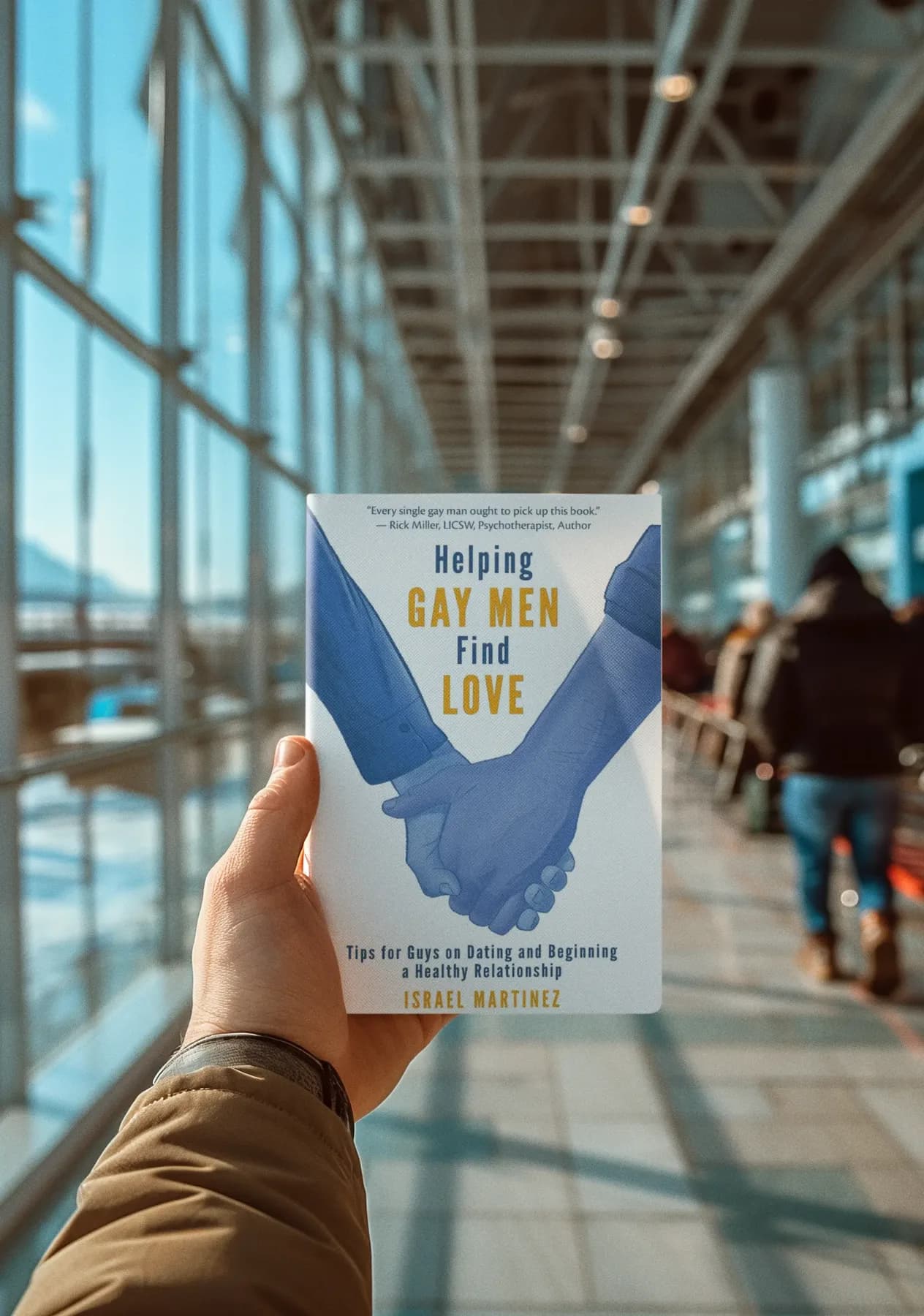 Hand holding the book Helping Gay Men Find Love at an airport