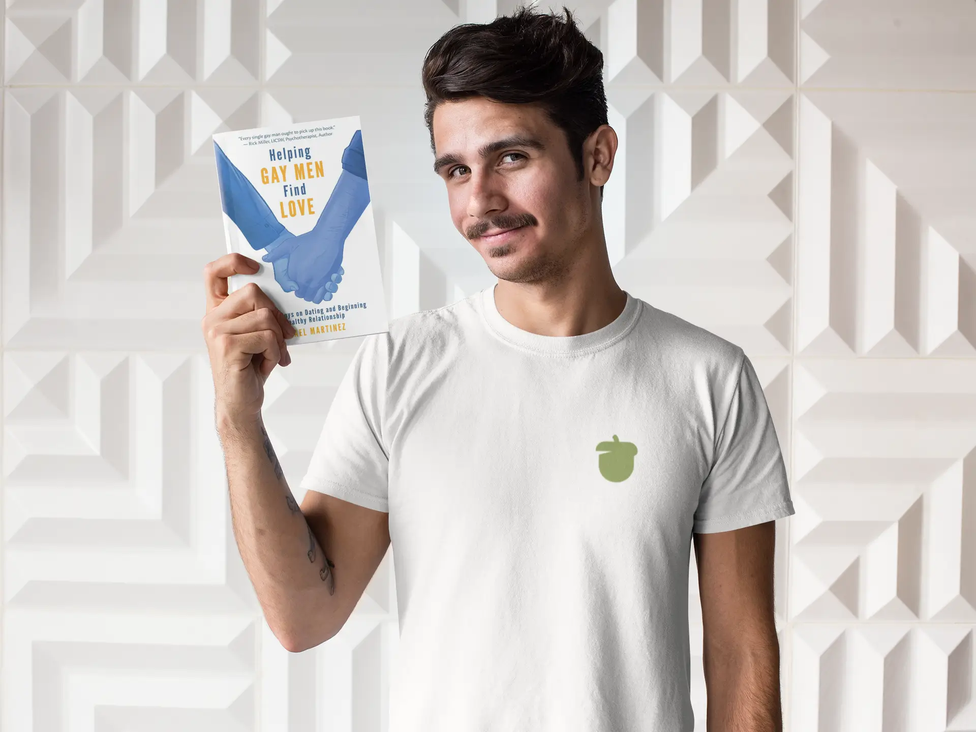 Man wearing a white tee holding the book Helping Gay Men Find Love by Dr. Israel Martinez